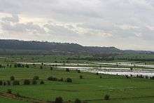 Water on grassy lowland with hills in the distance.