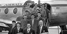 A black-and-white photograph of several people in suits and overcoats on the steps of an aircraft.
