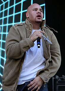 A bald man, wearing a white T-shirt and creamy pants is performing
