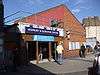 A red-bricked building with a rectangular, blue sign reading "HIGHBURY & ISLINGTON STATION" in white letters all under a blue sky with white clouds