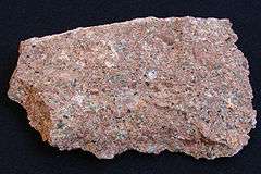 A rough chunk of granite showing grains of red, pink, white, gray and black.