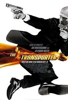 Jason Statham wearing a suit and holding two guns, in black and white. A band of orange colour with the title Transporter is overlaid in the middle of the picture.