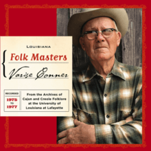 Varise standing with his arms crossed. He is wearing a green plaid shirt.